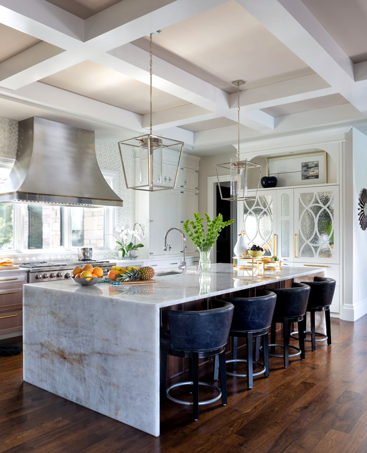 A large stone island sits amid a white kitchen with coffered ceilings and ornate woodworking. RED Winner.