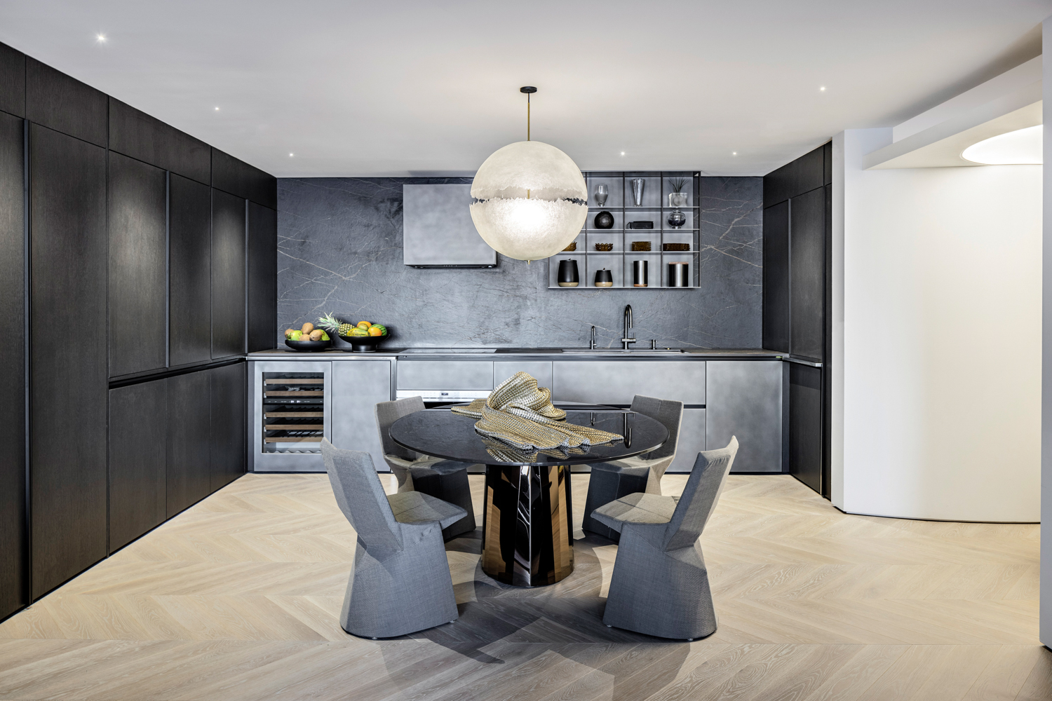 A round dining table with 4 sculptural chairs is in the middle of a modern metallic toned kitchen with hidden appliances. RED Winner.