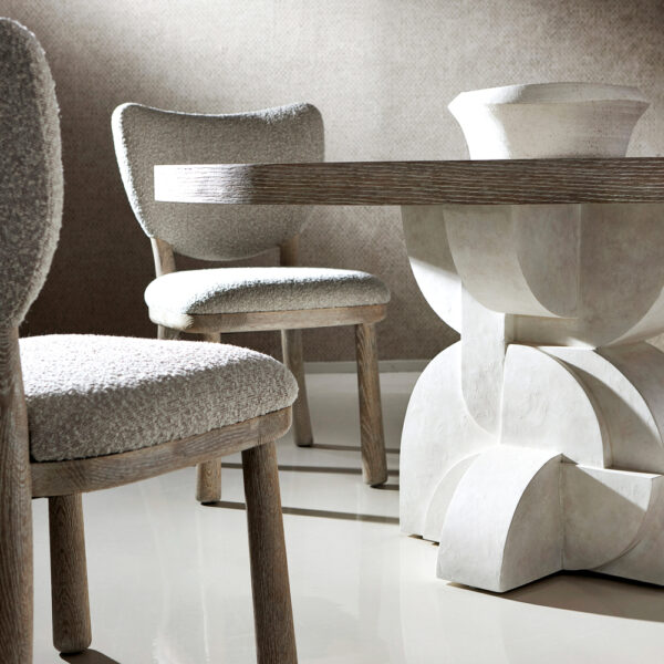 A neutral-toned dining table with a sculptural base. 2 dining chairs surround it. RED Winner.