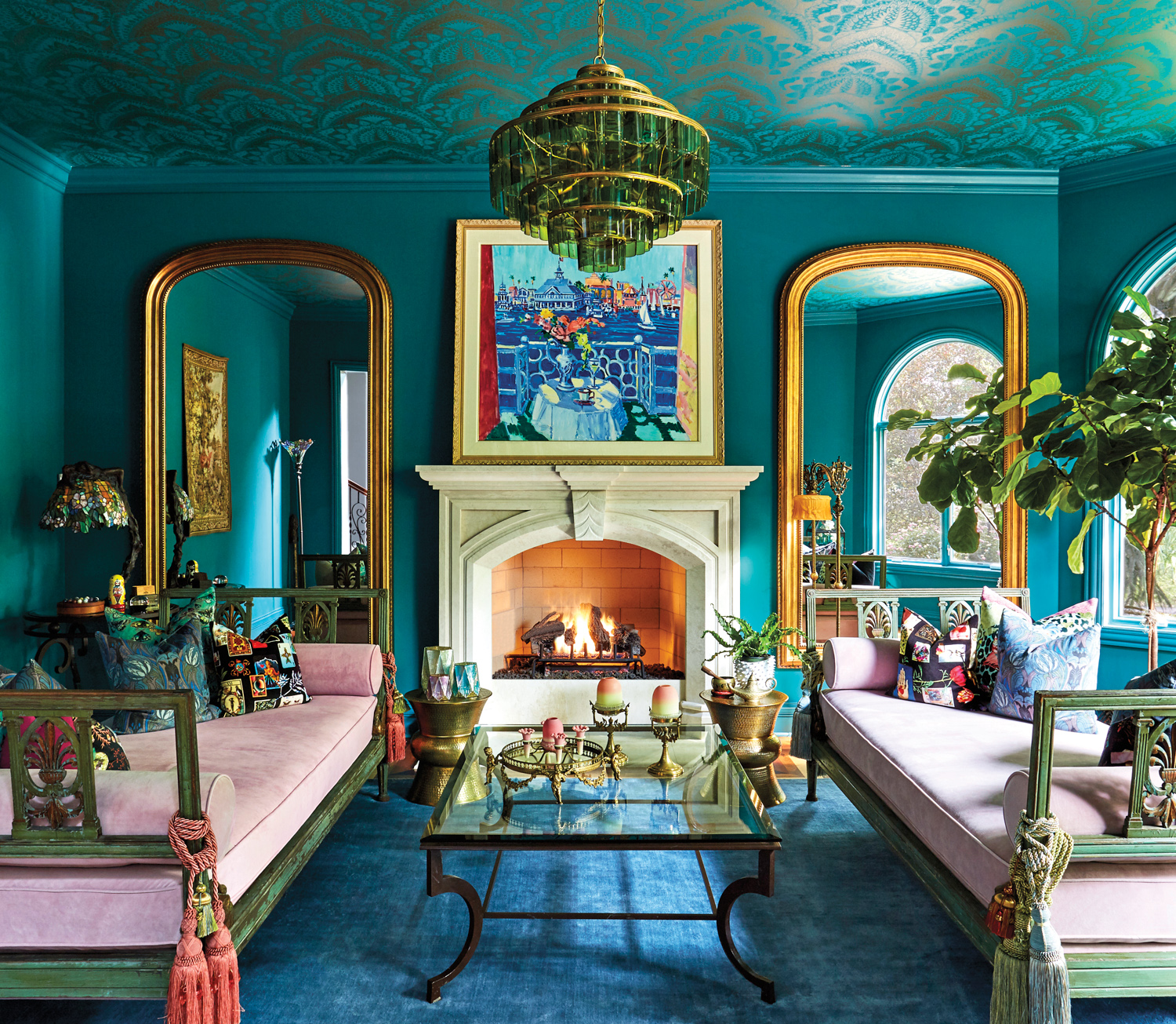 Two pink and green daybeds sit around a fireplace in an ornate teal room with brass accents. RED Winner.