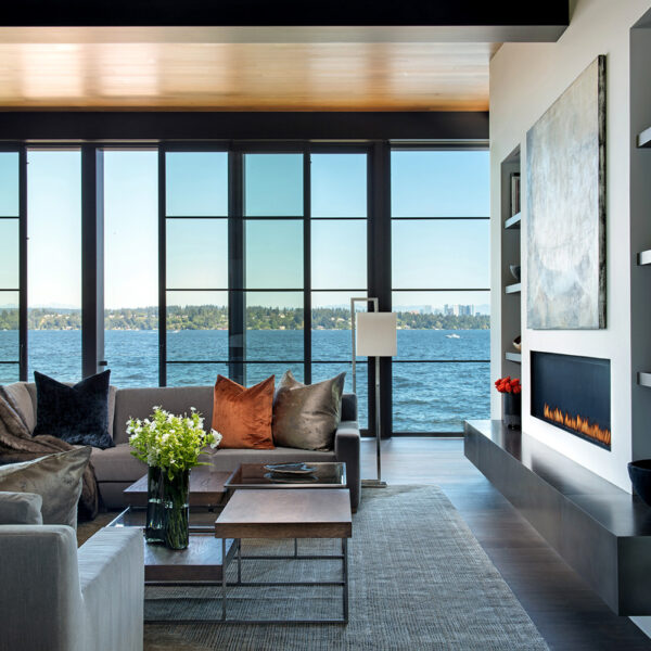 A modern grrey living room is lined with windows offering a scenic view. RED Winner.