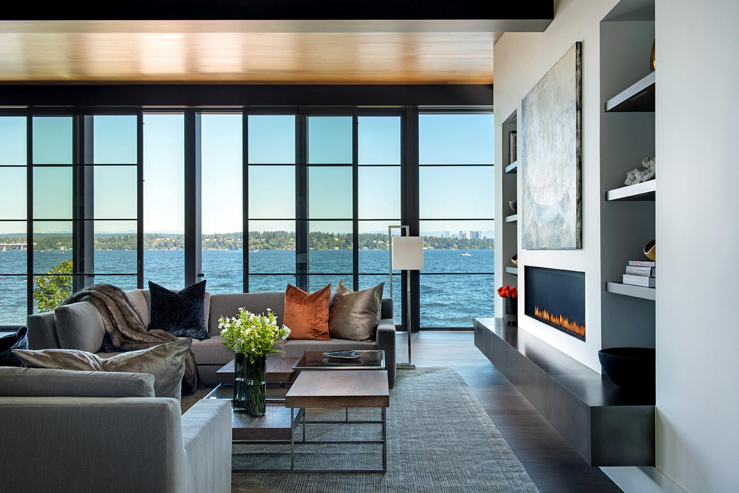 A modern grrey living room is lined with windows offering a scenic view. RED Winner.
