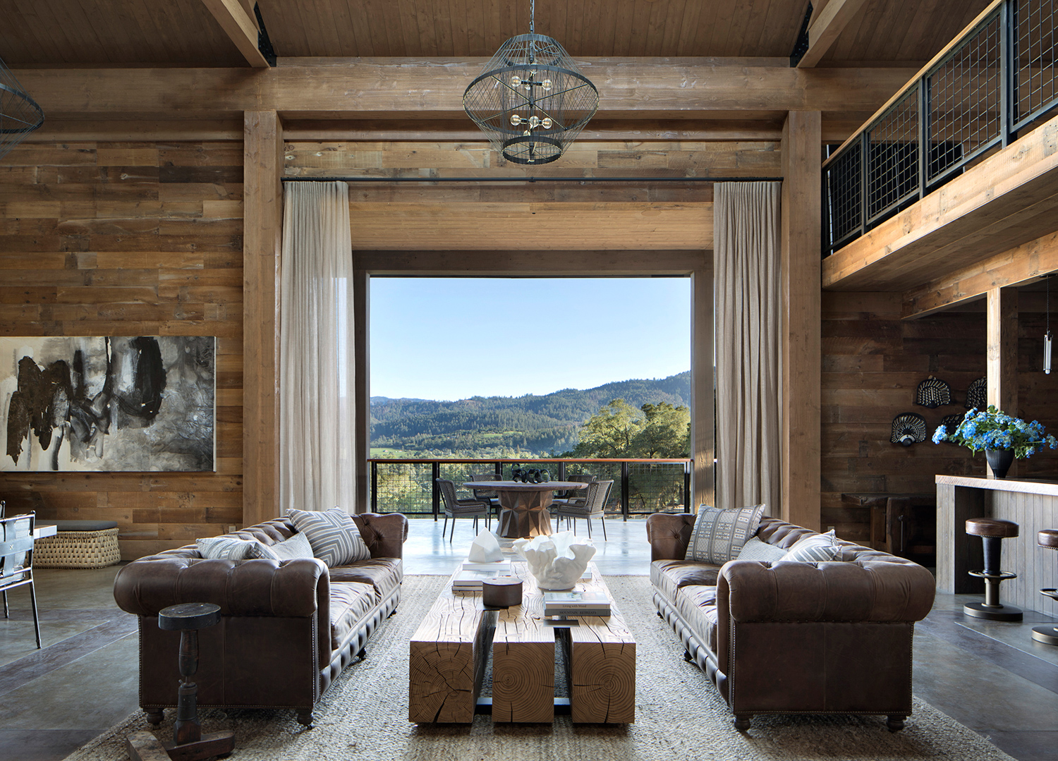 A wooden living room with leather sofas oepns up to an expansive outdoor patio. RED Winner.